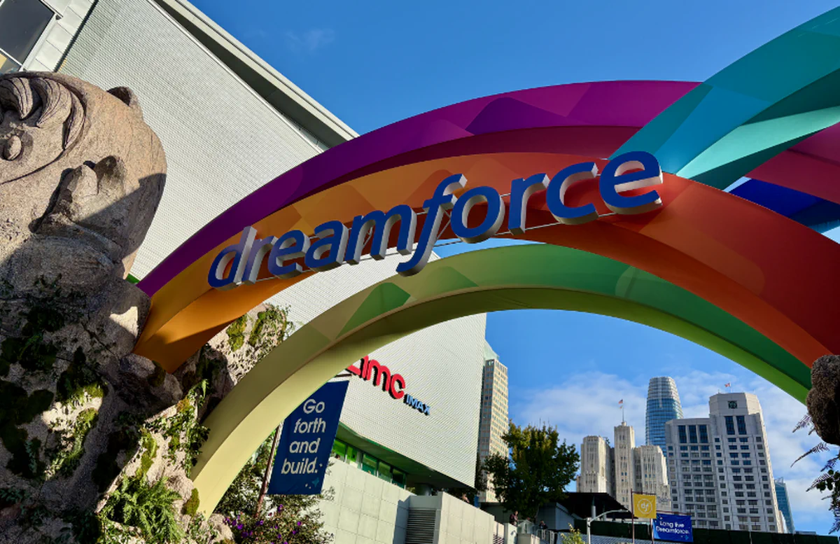 Colorful Dreamforce rainbow arch with ‘dreamforce’ lettering at the Moscone Center, San Francisco skyline visible in the background under a clear blue sky.